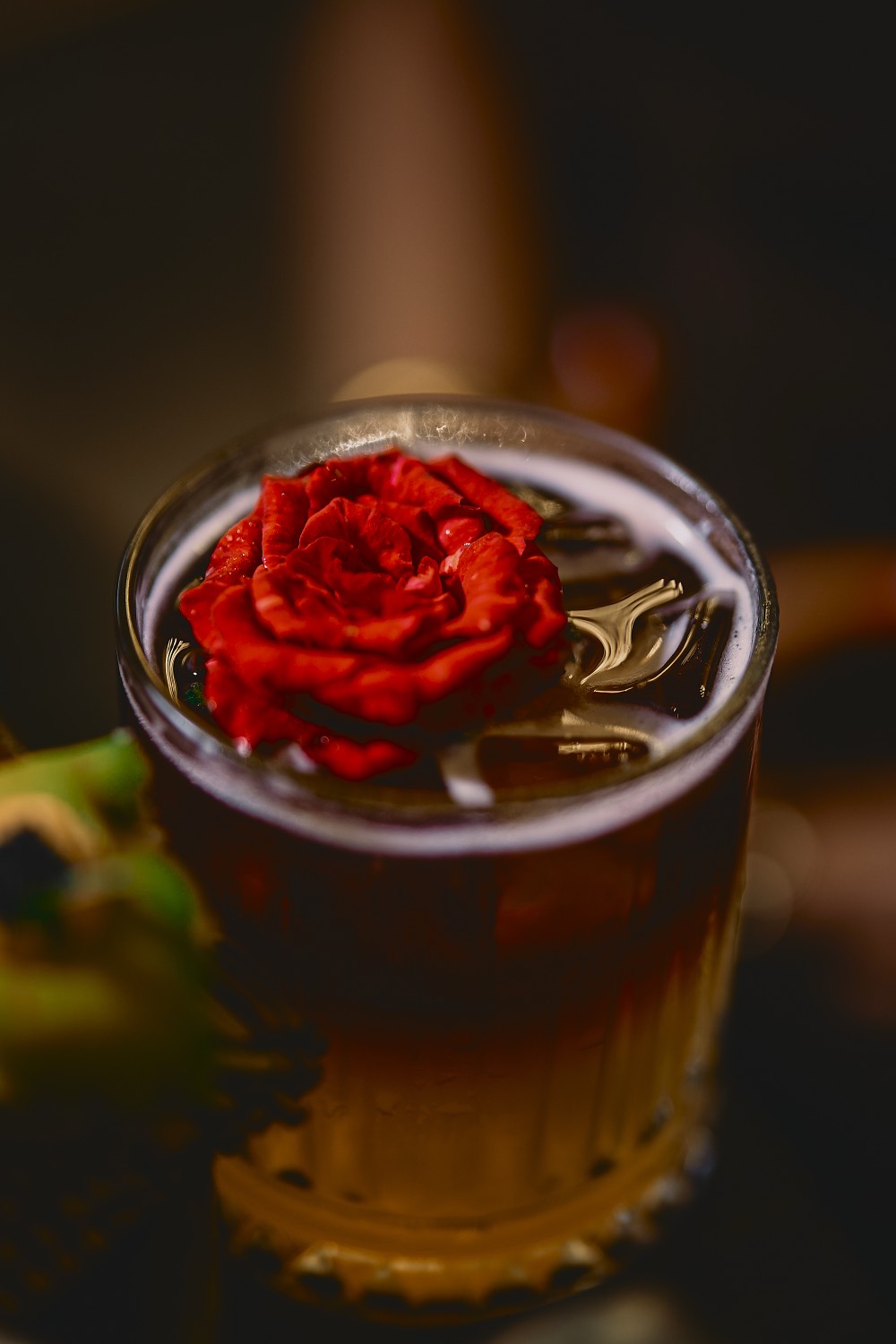 Signature cocktail crowned with a fresh red rose, served over ice