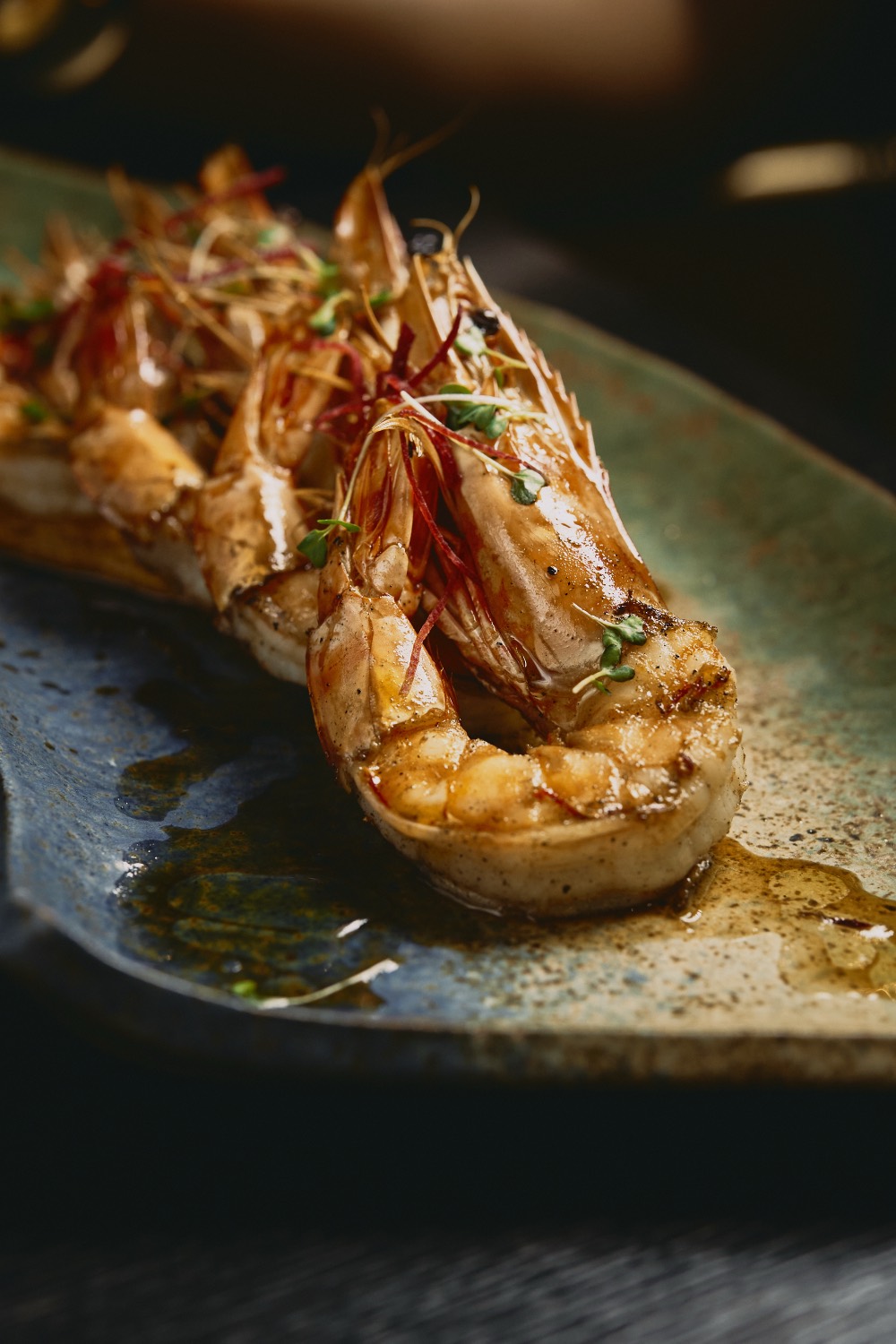 Fire-grilled tiger prawns with chili threads and micro herbs on artisan stoneware